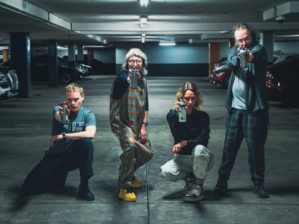 photograph in a dingy car park. four members of pvi collective are posing for the camera with spray cans at the ready
